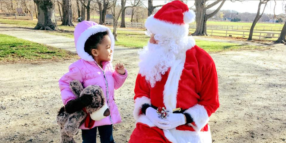 Photo of a young child smiling at a kneeling Santa Claus